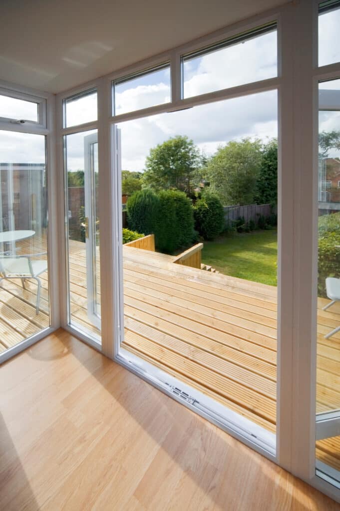 Terrasse bois et jardin vus d'un intérieur lumineux Intérieur lumineux avec plancher bois clair ouvrant sur une terrasse en bois et un jardin verdoyant par une porte-fenêtre entrouverte.